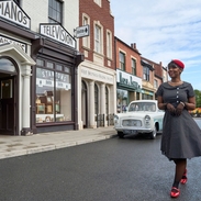 A woman posing in the street in front of shops and cars at a living museum