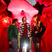 Three friends standing and laughing under a red illuminated canopy