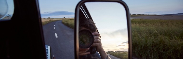 Reflection of man with camera in side view mirror of car