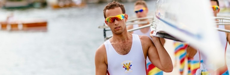 Rowers carrying a racing scull by the side of a river