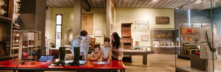 A man, a woman and two girls playing with touch screens inside a modern museum display.