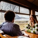 Couple, sat at a table inside train carriage, looking out