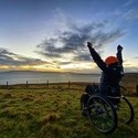 Wheelchair user, arms outstretched, watching the sunrise