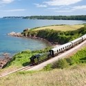 Steam train on railway line along coastline. Sea views