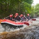 People wearing wetsuits and helmets paddling down a rapid