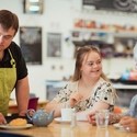 A person with Downs Syndrome serving customers in the cafe