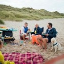 A family and their dog sat beside a picnic blanket on beach