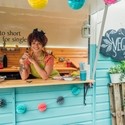 Young mixed race woman stood in the hatch of a food truck smiling, ready to serve