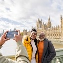 A man photographing mature couple with River Thames and Houses of Parliament in background.