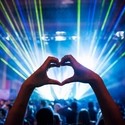 Woman making heart shape with hands at music event.