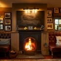 A fireplace with a lit fire flanked by two leather sofas with tables. The wall is covered in numerous framed artworks. The Duncombe Arms - Bronze award winner for the Pub of the Year at the VisitEngland Awards for Excellence 2023.