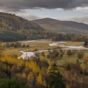 Landscape shot of a countryside view with a mountain backdrop and a stream running through the centre.