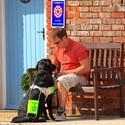 A man sat on a bench outside with his assistance dog